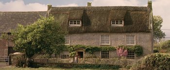 Movie still from “Tamara Drewe” (2010), directed by Stephen Frears – A person standing in front of a house with a fence; Extreme Wide shot, Low angle