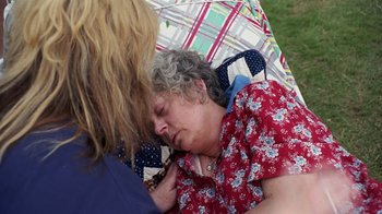 An older woman sleeping on the ground with another woman nearby