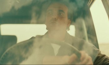 Movie still from “Taste of Cherry” (1997), directed by Abbas Kiarostami – A man sitting in the drivers seat of a car; Close Up shot, Low angle
