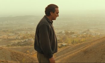 Movie still from “Taste of Cherry” (1997), directed by Abbas Kiarostami – A man standing on top of a hill looking at a city; Medium shot, Over the shoulder angle