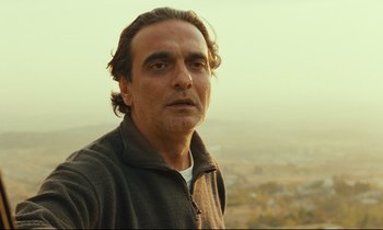 Movie still from “Taste of Cherry” (1997), directed by Abbas Kiarostami – A person wearing a jacket on a hill; Close Up shot, Low angle