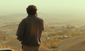 Movie still from “Taste of Cherry” (1997), directed by Abbas Kiarostami – A man standing on top of a hill talking on a cell phone; Wide shot, Over the shoulder angle