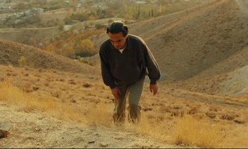 Movie still from “Taste of Cherry” (1997), directed by Abbas Kiarostami – A man is walking in a field of dry grass; Wide shot, Low angle