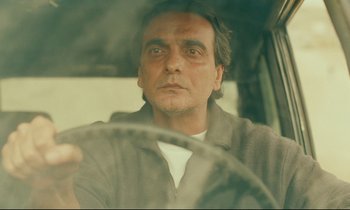 Movie still from “Taste of Cherry” (1997), directed by Abbas Kiarostami – A man sitting in the drivers seat of a car; Close Up shot, Low angle