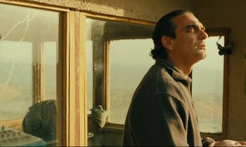Movie still from “Taste of Cherry” (1997), directed by Abbas Kiarostami – A man standing in front of a large window; Close Up shot, Low angle