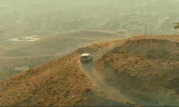 Movie still from “Taste of Cherry” (1997), directed by Abbas Kiarostami – A car driving down a dirt road in the middle of nowhere; Extreme Wide shot, High angle