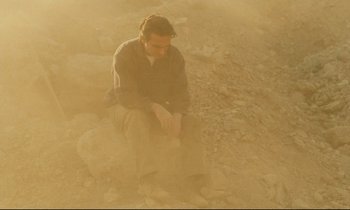 Movie still from “Taste of Cherry” (1997), directed by Abbas Kiarostami – A man sitting on the ground in the sand; Wide shot, Low angle