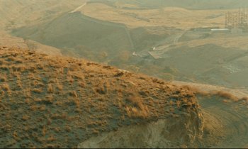 Movie still from “Taste of Cherry” (1997), directed by Abbas Kiarostami – An aerial view of a grassy area with a road in the background; Extreme Wide shot, High angle