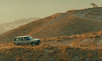 Movie still from “Taste of Cherry” (1997), directed by Abbas Kiarostami – A car driving down a dirt road in the desert; Extreme Wide shot, High angle