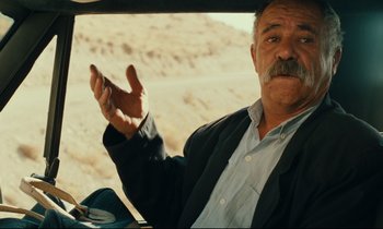 Movie still from “Taste of Cherry” (1997), directed by Abbas Kiarostami – An older man in a suit and tie driving a car; Close Up shot, Over the shoulder angle
