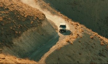 Movie still from “Taste of Cherry” (1997), directed by Abbas Kiarostami – An aerial view of a jeep driving down a dirt road; Extreme Wide shot, High angle