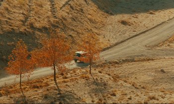 Movie still from “Taste of Cherry” (1997), directed by Abbas Kiarostami – A truck driving down a dirt road in the middle of a desert; Extreme Wide shot, High angle