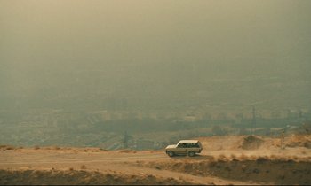 Movie still from “Taste of Cherry” (1997), directed by Abbas Kiarostami – A car driving down a dirt road in the middle of the desert; Extreme Wide shot, High angle