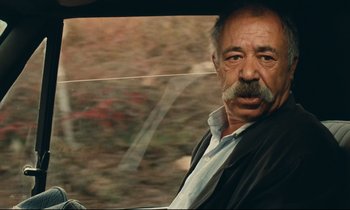 Movie still from “Taste of Cherry” (1997), directed by Abbas Kiarostami – An older man sitting in the driver's seat of a car; Close Up shot, Low angle