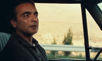 Movie still from “Taste of Cherry” (1997), directed by Abbas Kiarostami – A person in a car looking out the window; Close Up shot, Over the shoulder angle
