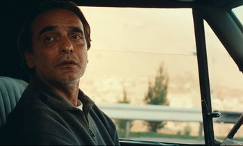 Movie still from “Taste of Cherry” (1997), directed by Abbas Kiarostami – A person sitting in a car looking out the window; Close Up shot, Over the shoulder angle