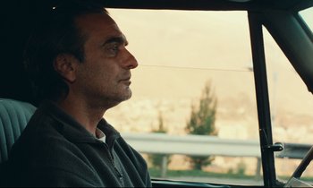 Movie still from “Taste of Cherry” (1997), directed by Abbas Kiarostami – A man sitting in the driver's seat of a car looking out the window; Close Up shot, Over the shoulder angle