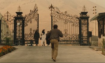 Movie still from “Taste of Cherry” (1997), directed by Abbas Kiarostami – A man is walking through a gate with people; Extreme Wide shot, High angle