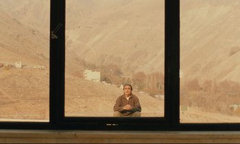 Movie still from “Taste of Cherry” (1997), directed by Abbas Kiarostami – A man sitting in front of a window with a mountain view; Wide shot, Over the shoulder angle
