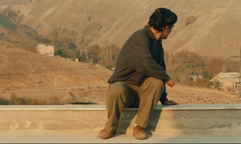 Movie still from “Taste of Cherry” (1997), directed by Abbas Kiarostami – A man sitting on the edge of a wall; Wide shot, High angle