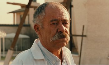 Movie still from “Taste of Cherry” (1997), directed by Abbas Kiarostami – An older man with a mustache is looking at the camera; Close Up shot, Low angle