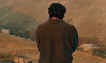 Movie still from “Taste of Cherry” (1997), directed by Abbas Kiarostami – A man standing in front of a mountain range; Medium shot, Low angle