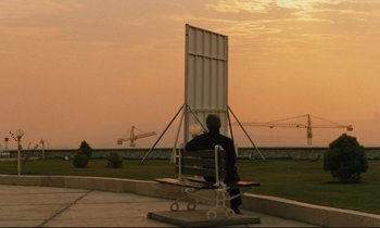 Movie still from “Taste of Cherry” (1997), directed by Abbas Kiarostami – A man sitting on a bench in front of an airplane; Extreme Wide shot, Low angle