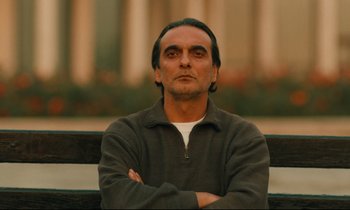 Movie still from “Taste of Cherry” (1997), directed by Abbas Kiarostami – A man sitting on top of a bench with his arms crossed; Close Up shot, Low angle