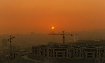 Movie still from “Taste of Cherry” (1997), directed by Abbas Kiarostami – An orange sun setting over a city with a crane in the foreground; Extreme Wide shot, Low angle