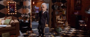 Movie still from “Team America: World Police” (2004), directed by Trey Parker – A man in a suit holding a briefcase in a room; Wide shot, Low angle