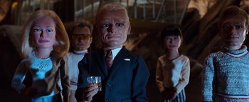 Movie still from “Team America: World Police” (2004), directed by Trey Parker – A man in a suit and tie holding a glass of wine; Medium shot, Low angle