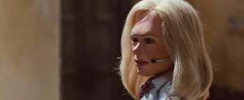 Movie still from “Team America: World Police” (2004), directed by Trey Parker – A woman with blonde hair is wearing a suit and tie; Close Up shot, High angle