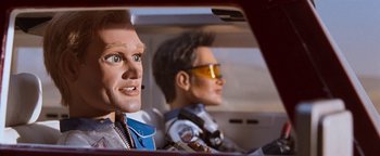 Movie still from “Team America: World Police” (2004), directed by Trey Parker – A doll in a car with another doll in the back seat; Close Up shot, Low angle