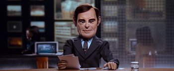 Movie still from “Team America: World Police” (2004), directed by Trey Parker – A man in a business suit sitting at a desk with papers; Close Up shot, Low angle