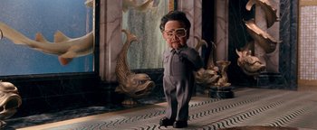 Movie still from “Team America: World Police” (2004), directed by Trey Parker – A man in a gray suit standing in front of two fish; Medium shot, Low angle