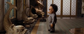 Movie still from “Team America: World Police” (2004), directed by Trey Parker – A man is standing in front of a statue of fish; Medium shot, High angle