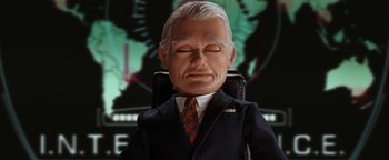 Movie still from “Team America: World Police” (2004), directed by Trey Parker – A man in a suit and tie sitting in an office chair; Close Up shot, Low angle