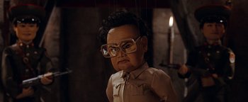 Movie still from “Team America: World Police” (2004), directed by Trey Parker – A puppet of a man wearing glasses and a tan shirt; Close Up shot, Low angle