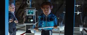 Movie still from “Team America: World Police” (2004), directed by Trey Parker – A man in a blue jacket is holding a barbell; Medium shot, Low angle