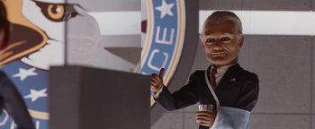 Movie still from “Team America: World Police” (2004), directed by Trey Parker – A man in a black suit holding a drink; Medium shot, Low angle