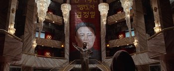 Movie still from “Team America: World Police” (2004), directed by Trey Parker – A statue in front of a staircase with a large poster of a man in front of it; Wide shot, Low angle