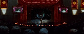 Movie still from “Team America: World Police” (2004), directed by Trey Parker – A man standing on a stage in front of a curtain; Extreme Wide shot, High angle