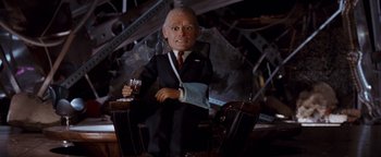 Movie still from “Team America: World Police” (2004), directed by Trey Parker – A man in a suit and tie holding a glass of wine; Medium shot, Low angle