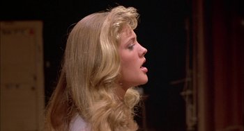 Movie still from “Teen Wolf” (1985), directed by Rod Daniel – A woman with long blonde hair is singing a song; Close Up shot, Over the shoulder angle