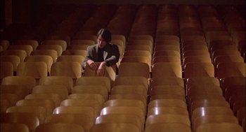 Movie still from “Teen Wolf” (1985), directed by Rod Daniel – A man sitting in a room full of chairs; Wide shot, High angle