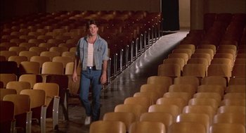 Movie still from “Teen Wolf” (1985), directed by Rod Daniel – A man walking in front of rows of empty chairs; Wide shot, High angle