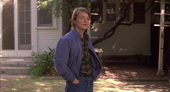 Movie still from “Teen Wolf” (1985), directed by Rod Daniel – A man standing in front of a house with his hands in his pockets; Medium shot, Over the shoulder angle
