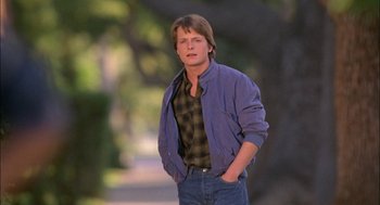 Movie still from “Teen Wolf” (1985), directed by Rod Daniel – A man standing on the side of a road with his hands in his pockets; Medium shot, Low angle
