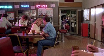 Movie still from “Teen Wolf” (1985), directed by Rod Daniel – A man and a woman sitting at a table in front of a hot dog stand; Wide shot, Over the shoulder angle