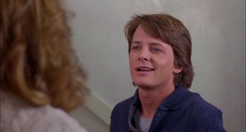 Movie still from “Teen Wolf” (1985), directed by Rod Daniel – A young man with long brown hair is smiling at the camera; Close Up shot, Over the shoulder angle